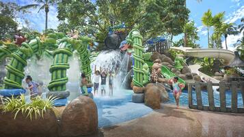 Experience the thrill of a tropical water park with a large waterfall and slide surrounded by lush greenery and palm trees.