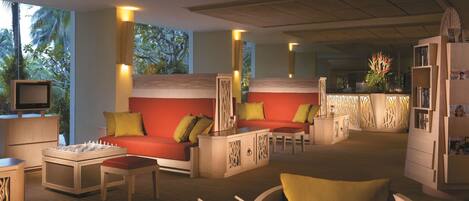 A hotel lobby with a red sofa, a chess table, and a bar area with a decorative plant.
