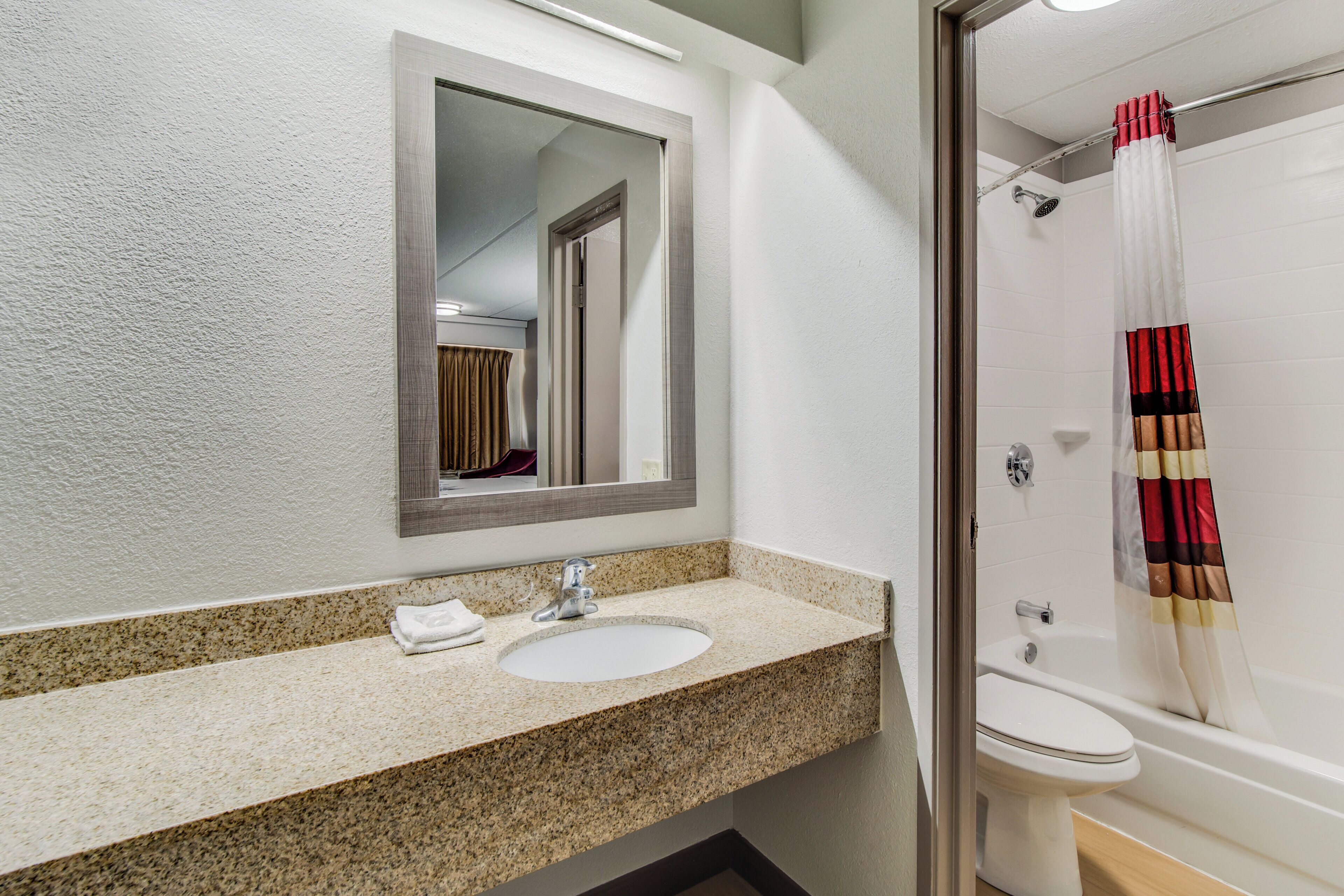 A bathroom with a granite countertop sink, a mirror, a shower with a striped curtain, and a toilet.