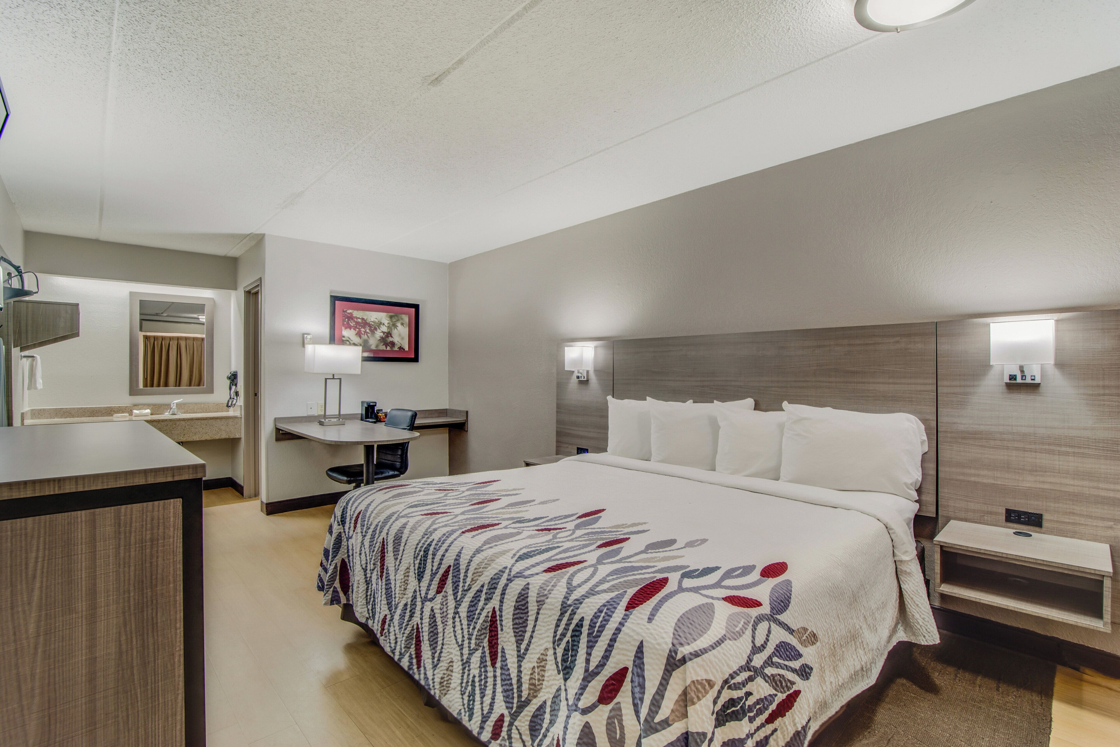 A hotel room with a bed, bedside table, desk, and a bathroom.