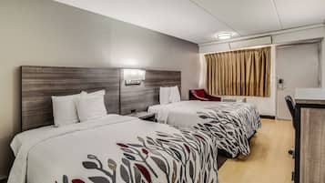 A hotel room with two beds, a desk, a chair, and a bathroom door.