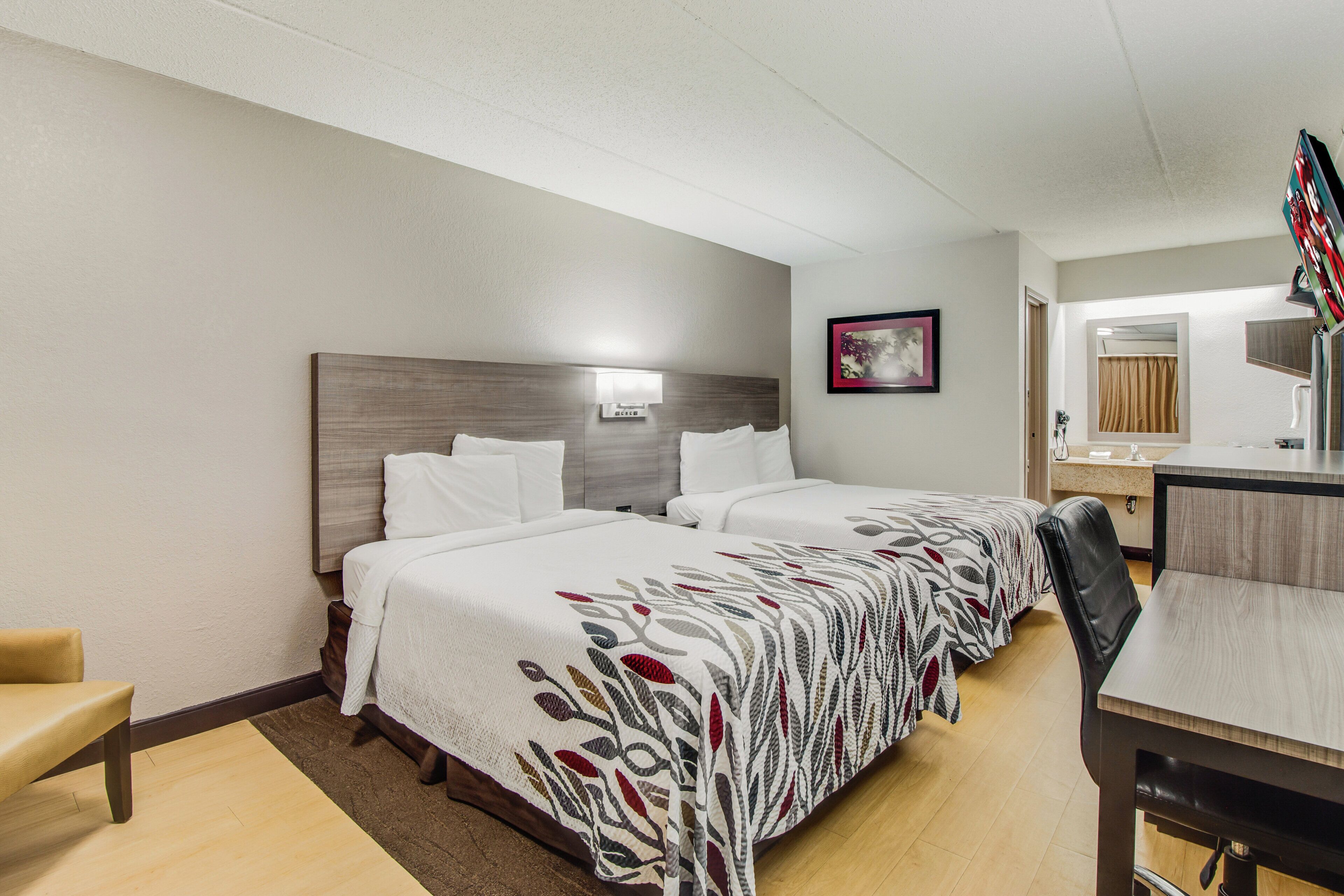 A hotel room with two beds, a desk, a chair, and a bathroom mirror.