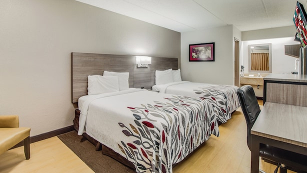 A hotel room with two beds, a desk, a chair, and a bathroom mirror.