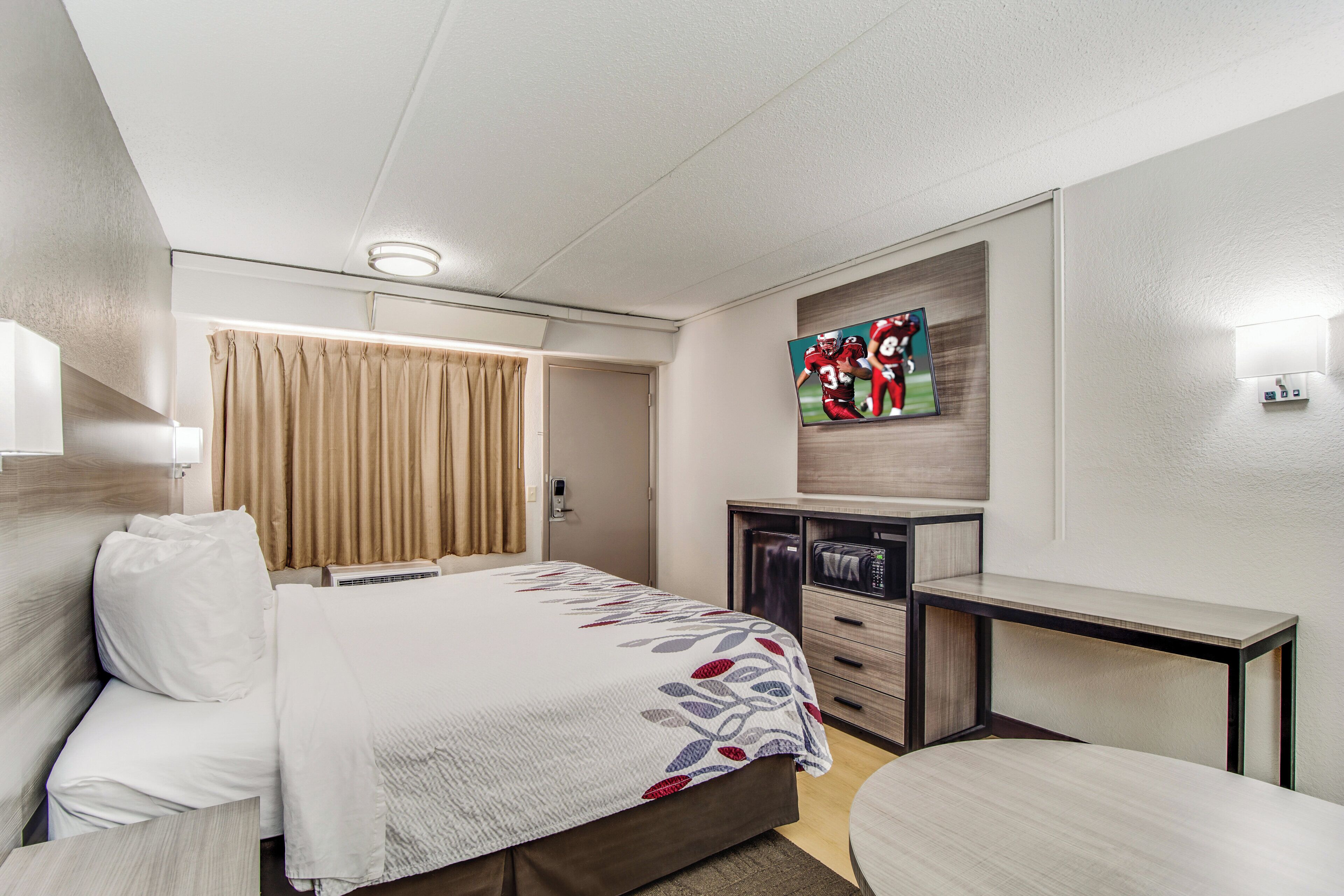 A hotel room with a bed, a desk, a flat-screen TV, a wardrobe, and a door.