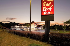 A Red Roof Inn sign with a parking lot and a building in the background. - Red Roof Inn Columbia East - Ft Jackson (Columbia)