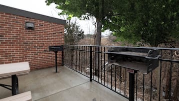 Een terras buiten met een barbecue, een tafel en een bakstenen muur.