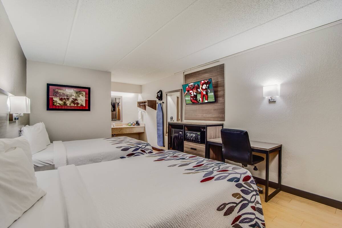 Habitación de hotel con dos camas, un escritorio, una silla, un televisor y un cuadro en la pared.