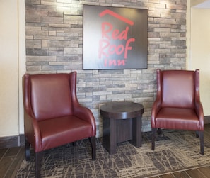 Two leather armchairs and a small table in a room with a stone wall and a Red Roof Inn sign. - Red Roof Inn Columbia East - Ft Jackson (Columbia)