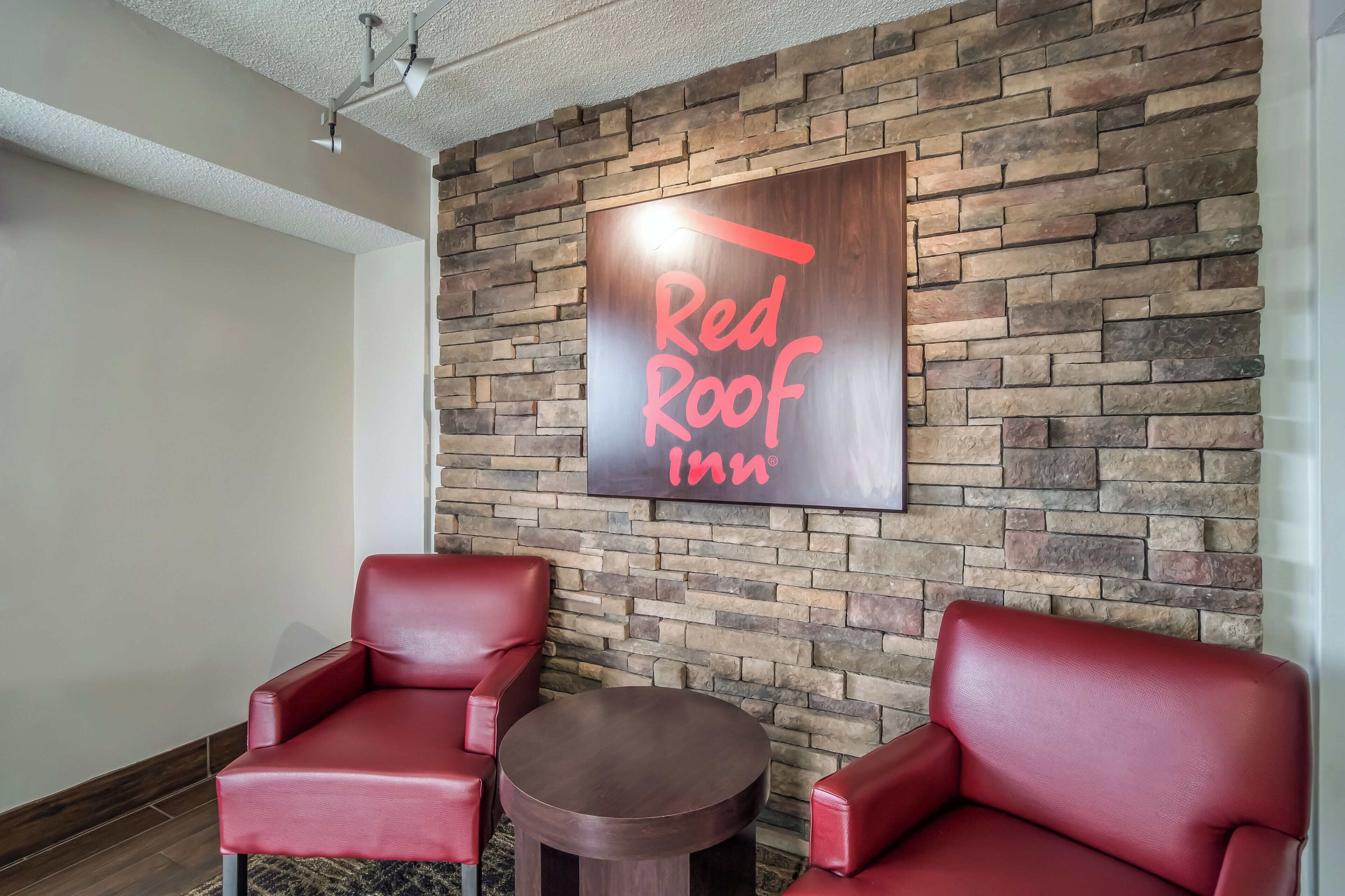 A Red Roof Inn sign on a stone wall, two red leather chairs, and a small round table.