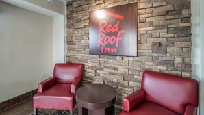 A Red Roof Inn sign on a stone wall, two red leather chairs, and a small round table.
