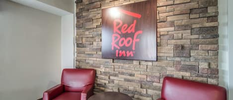 Segnaletica Red Roof Inn su un muro in pietra, due poltrone in pelle rossa e un piccolo tavolino rotondo.