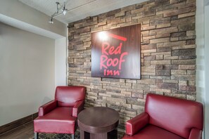 A Red Roof Inn sign on a stone wall, two red leather chairs, and a small round table. - Red Roof Inn Columbia East - Ft Jackson (Columbia)
