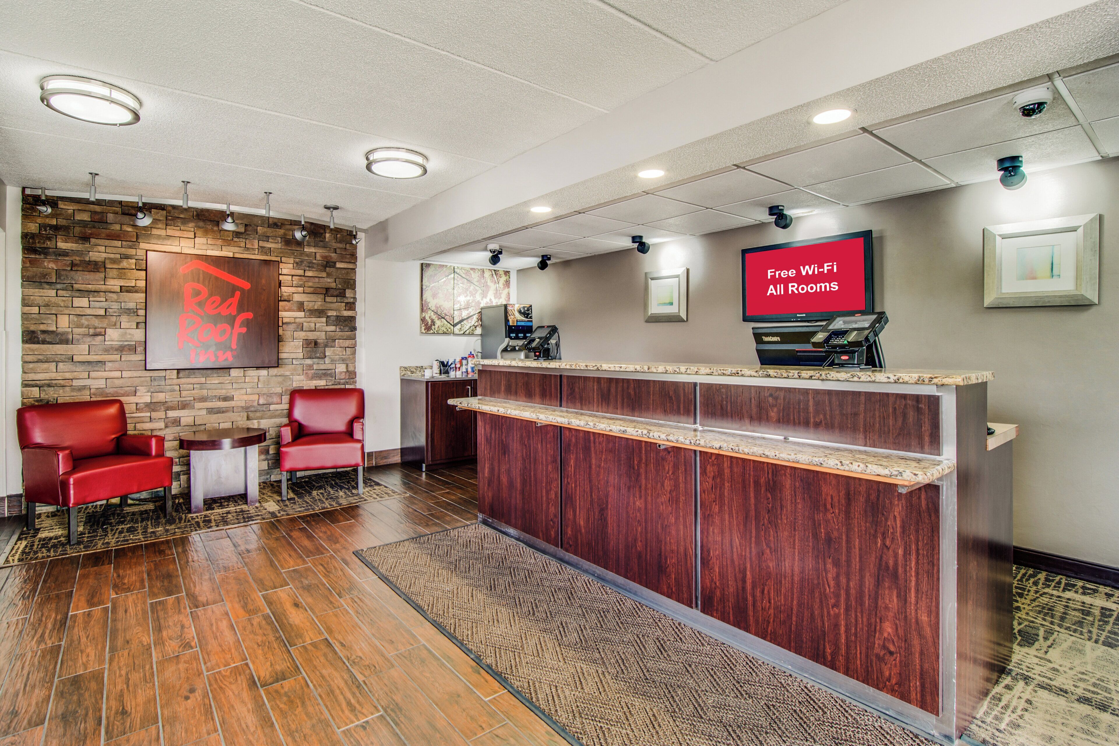 A reception area with a Red Roof Inn sign, a reception desk, a TV screen advertising free Wi-Fi, and a seating area with chairs.