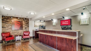 A reception area with a Red Roof Inn sign, a reception desk, a TV screen advertising free Wi-Fi, and a seating area with chairs.