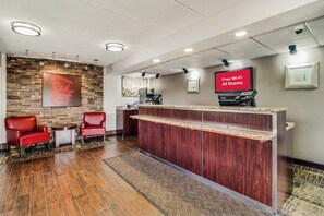 A reception area with a Red Roof Inn sign, a reception desk, a TV screen advertising free Wi-Fi, and a seating area with chairs. - Red Roof Inn Columbia East - Ft Jackson (Columbia)