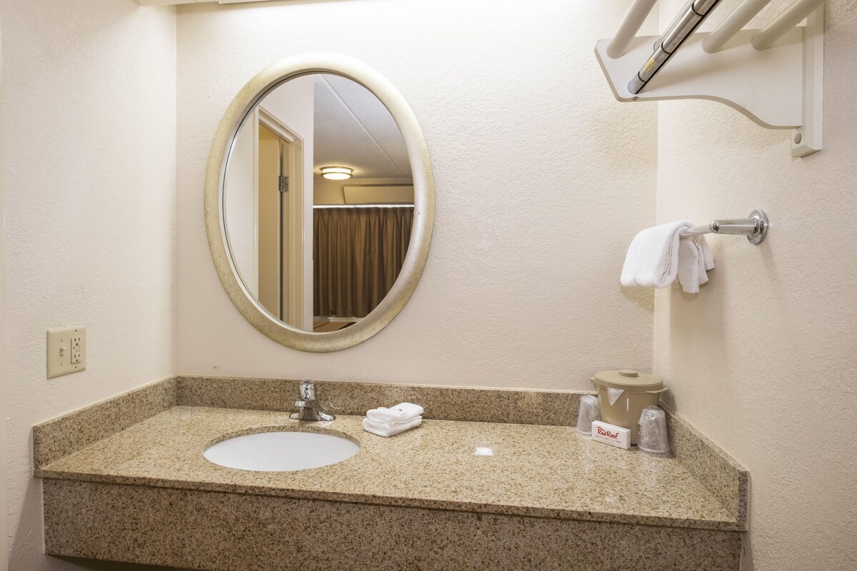 Un baño con encimera de granito, un espejo redondo, un lavabo, un perchero para toallas y un dispensador de papel higiénico.