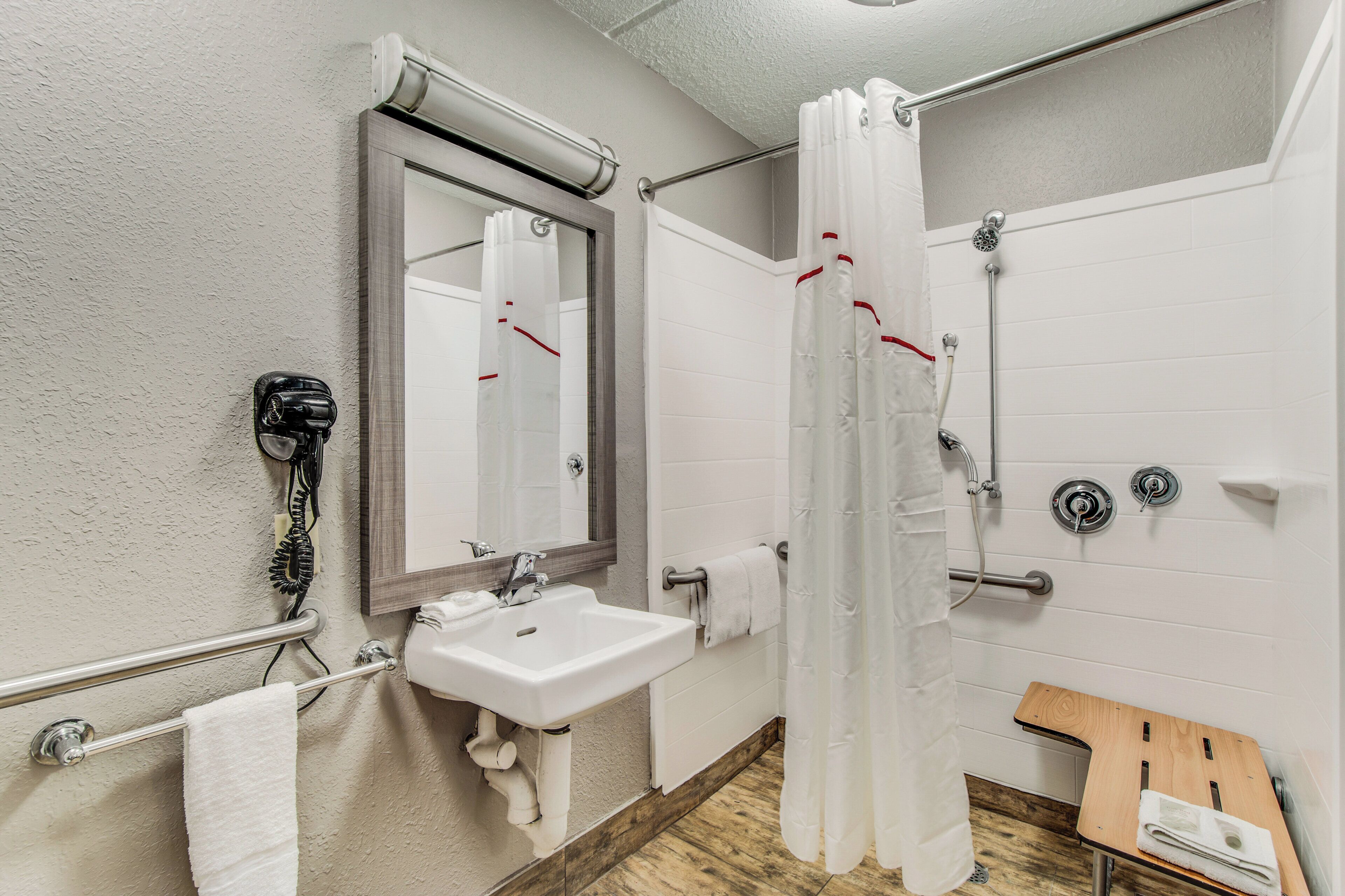 Ein Badezimmer mit einem weißen Waschbecken, einem Spiegel, einer Duschkabine und einer hölzernen Sitzbank.