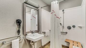 Ein Badezimmer mit einem weißen Waschbecken, einem Spiegel, einer Duschkabine und einer hölzernen Sitzbank.
