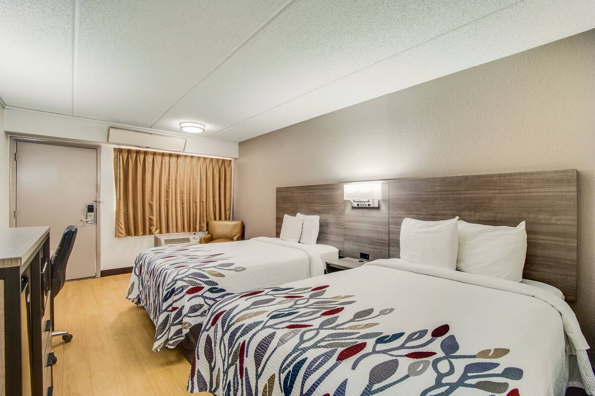 A hotel room with two beds, a desk, and a chair.