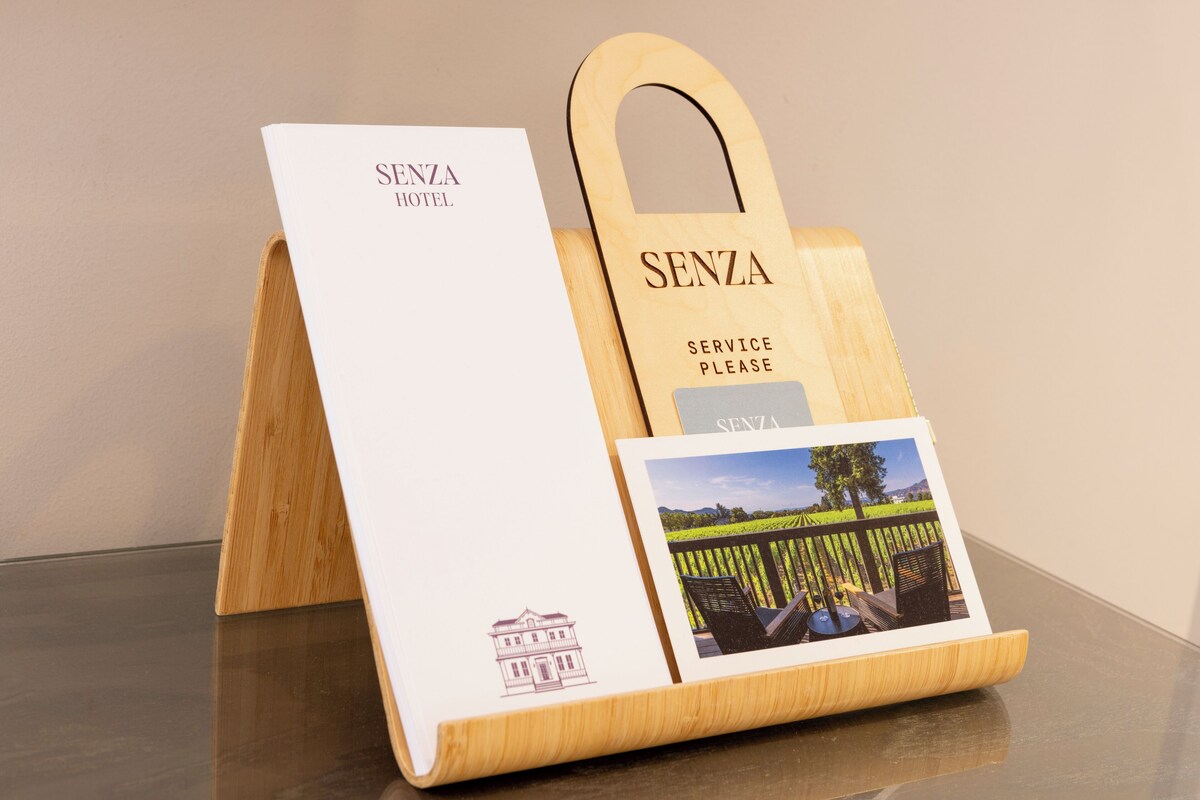 Une plaque en bois indiquant les services de l’hôtel, avec l’inscription « SENZA HOTEL » et une photo d’un espace extérieur pittoresque.