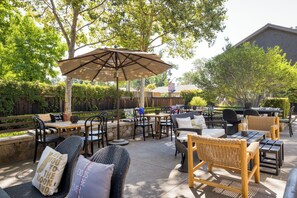 Relax in a serene outdoor space surrounded by lush greenery, with wicker chairs, a sofa, and a dining table.