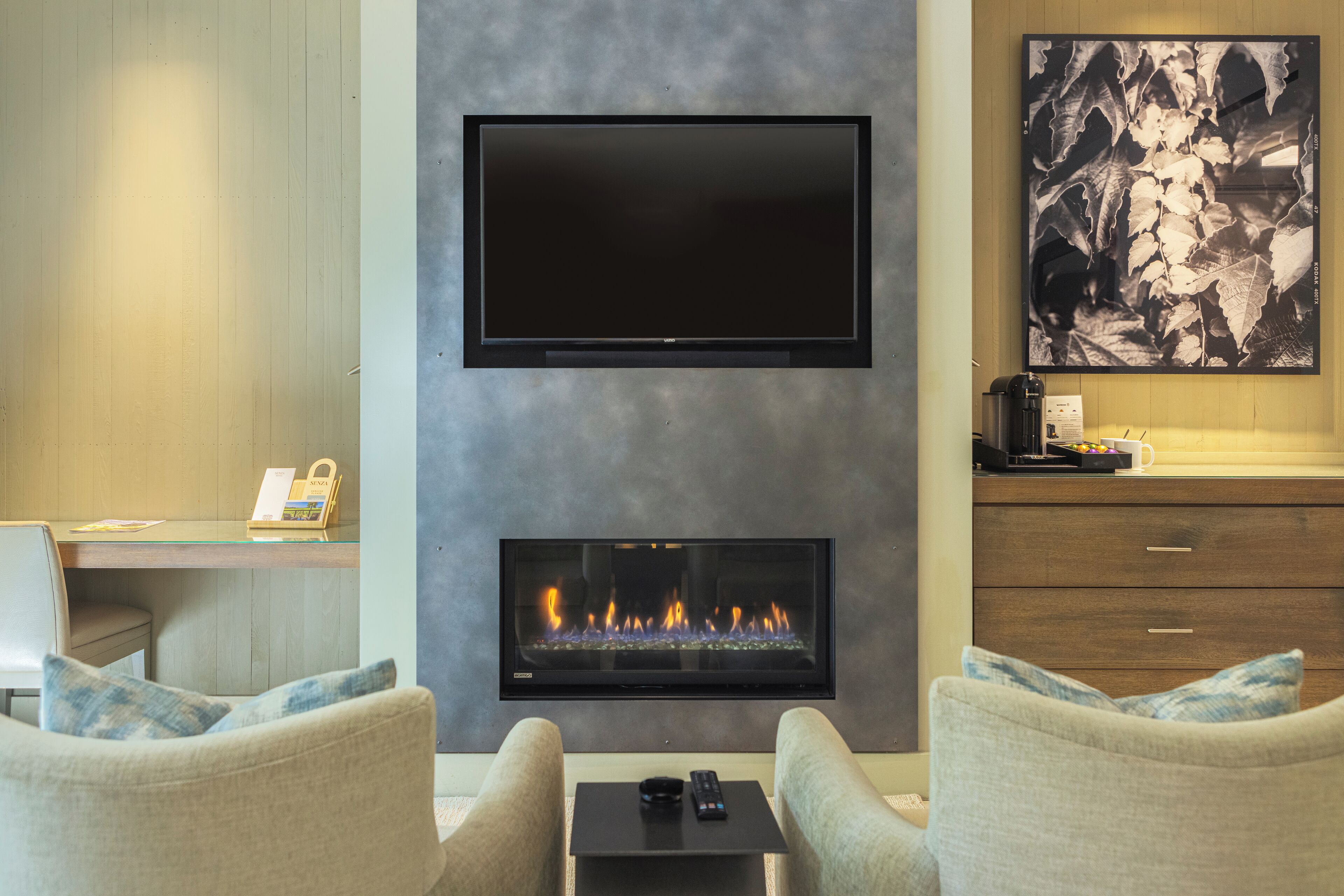 Una sala de estar moderna con un televisor de pantalla plana sobre la chimenea, dos sofás, una mesa de centro y un escritorio con una computadora y un teléfono.
