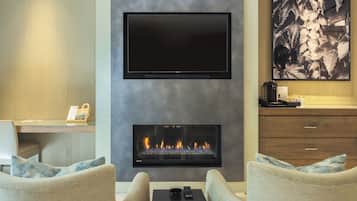 Una sala de estar moderna con un televisor de pantalla plana sobre la chimenea, dos sofás, una mesa de centro y un escritorio con una computadora y un teléfono.