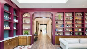 Un interior moderno con un vestíbulo central que conduce a una sala de estar, con armarios de madera, un sofá blanco y estantes con diversos objetos decorativos.