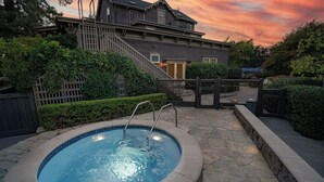 Una piscina con sol árium de piedra, rodeada por una valla de madera y abundante vegetación.