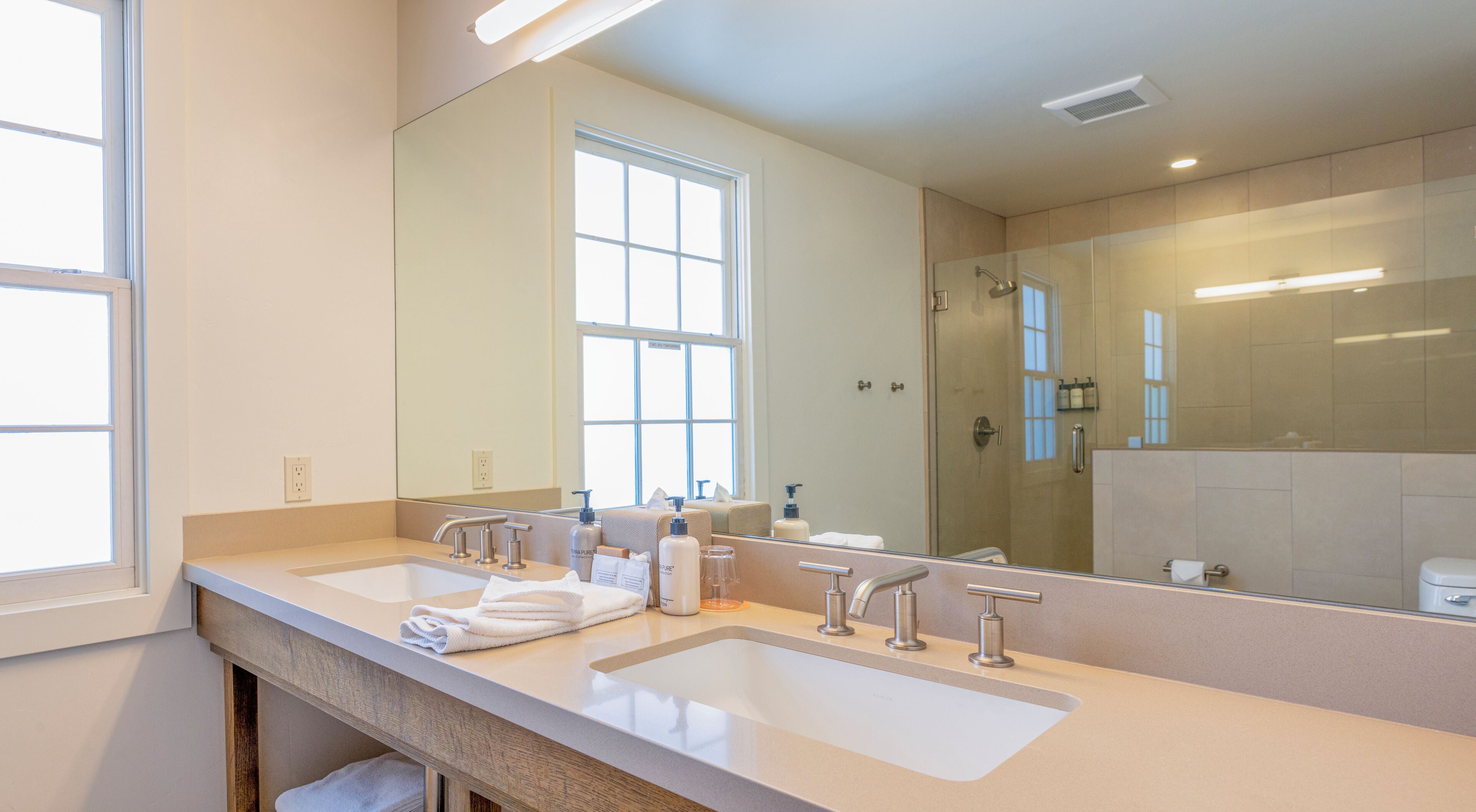 A modern bathroom with two sinks, a large mirror, and a glass-enclosed shower.