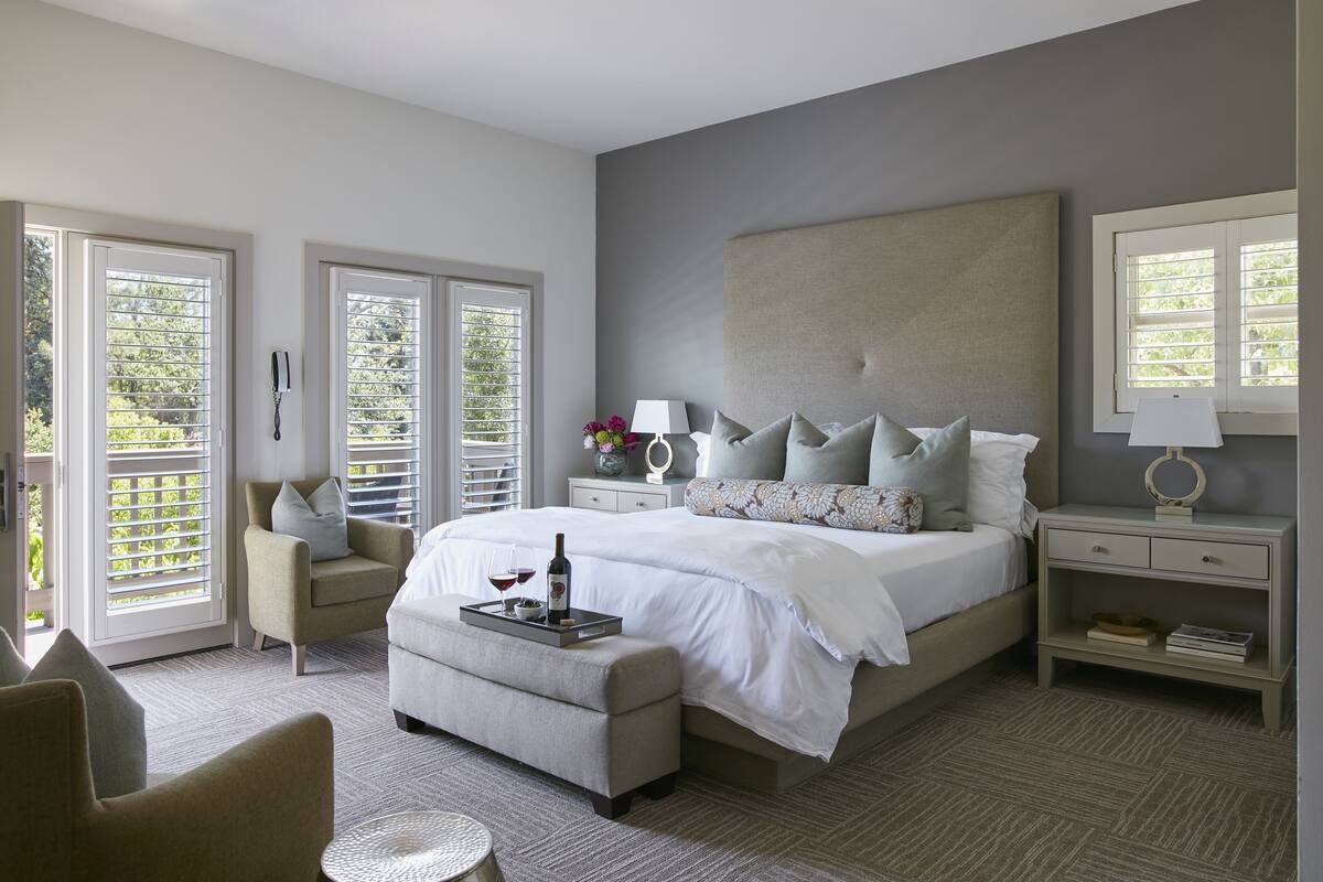 A bedroom with a large bed, a bedside table with a lamp, a chair, and a small table with a tray.