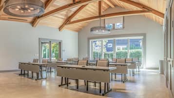 A spacious conference room with high ceilings and large windows, featuring multiple tables and chairs.