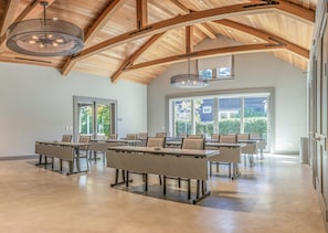 A spacious conference room with high ceilings and large windows, featuring multiple tables and chairs.
