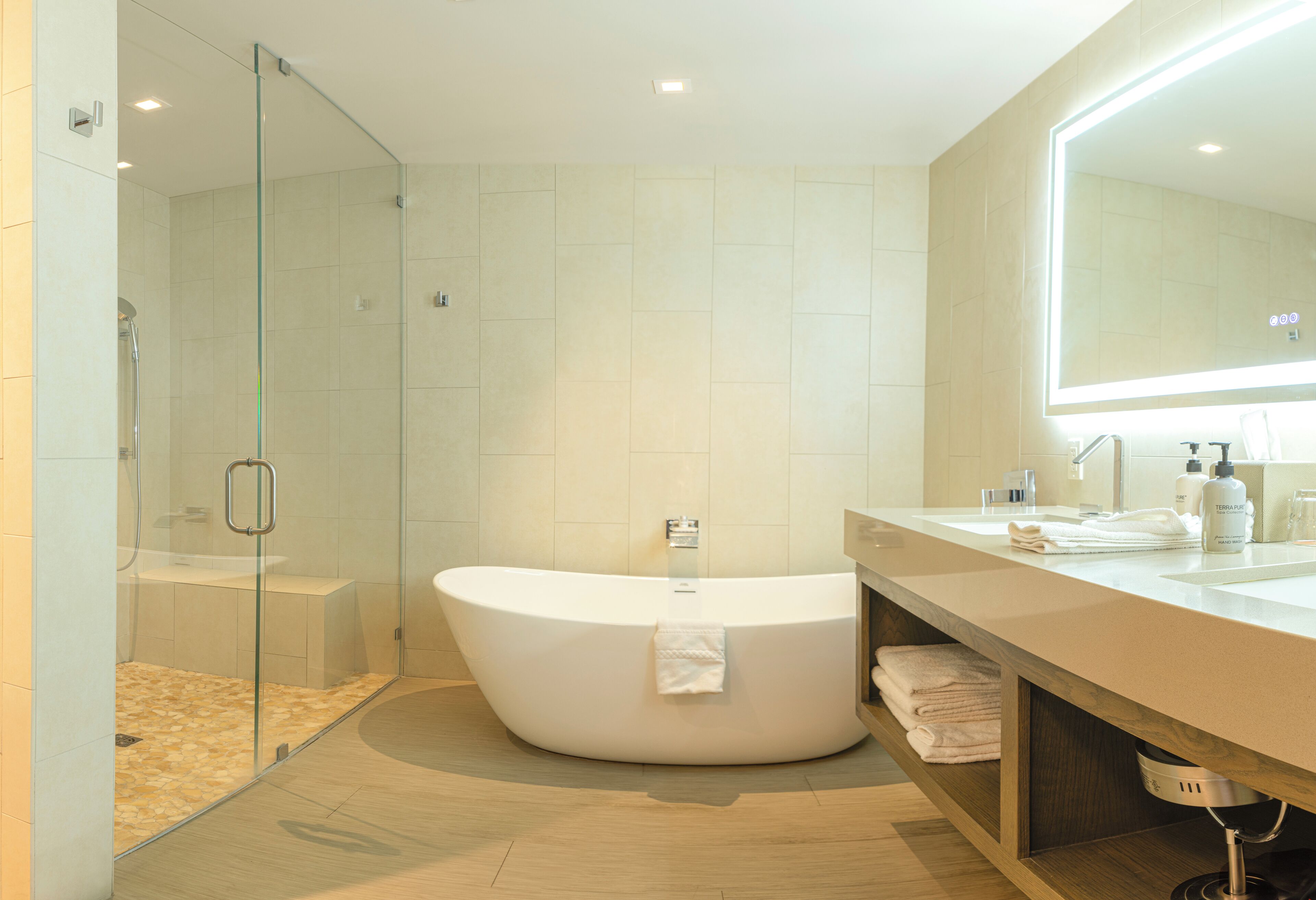 Ein modernes Badezimmer mit freistehender Badewanne, einer ein Glaswand abgetrennten Dusche und einem Waschtisch mit großem Spiegel.