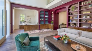 Una sala moderna con un sillón verde, un sofá beige y una mesita de centro con libros y un jarrón de flores.