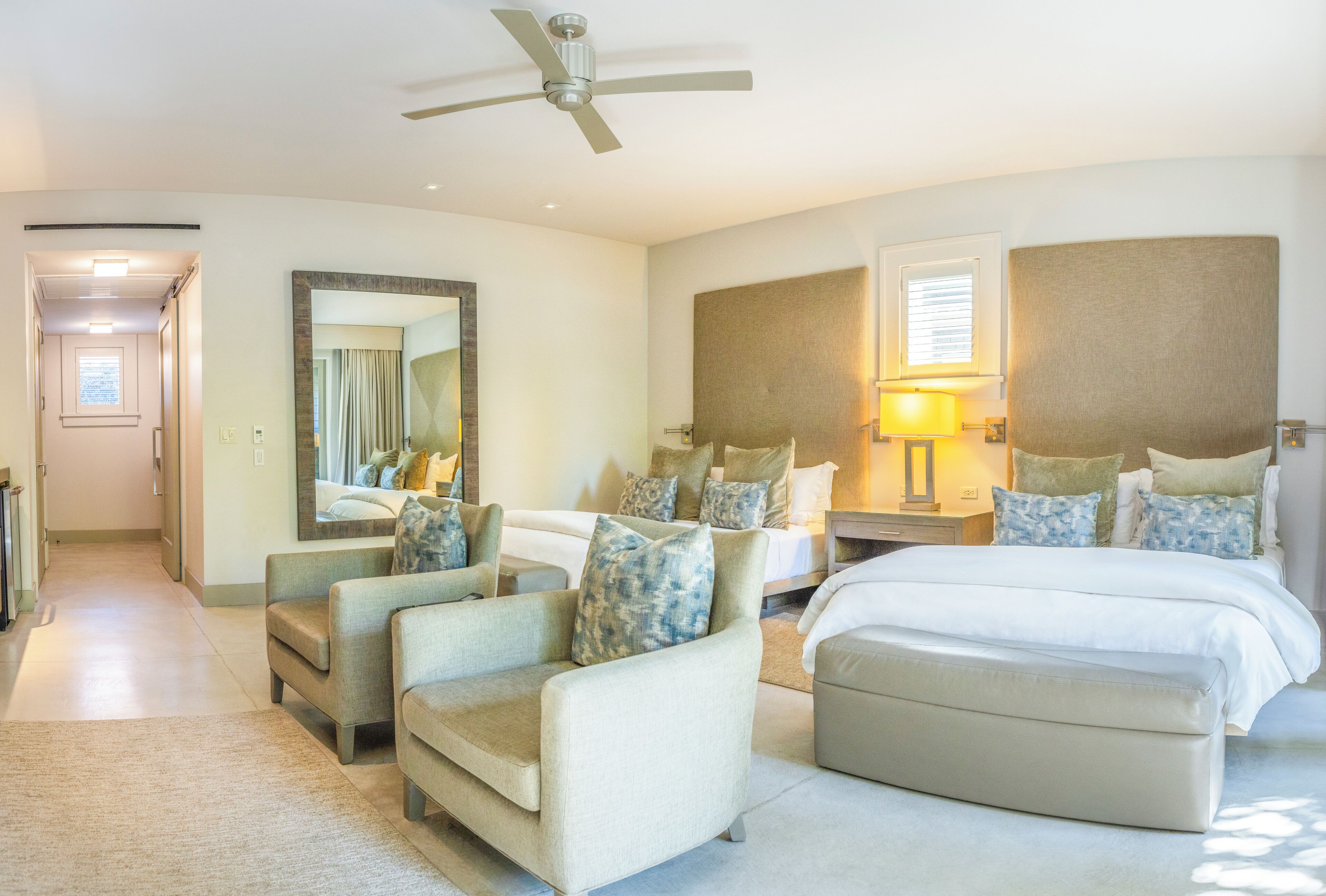 A hotel room with a bed, two armchairs, a sofa, a nightstand, a lamp, a ceiling fan, and a large mirror.