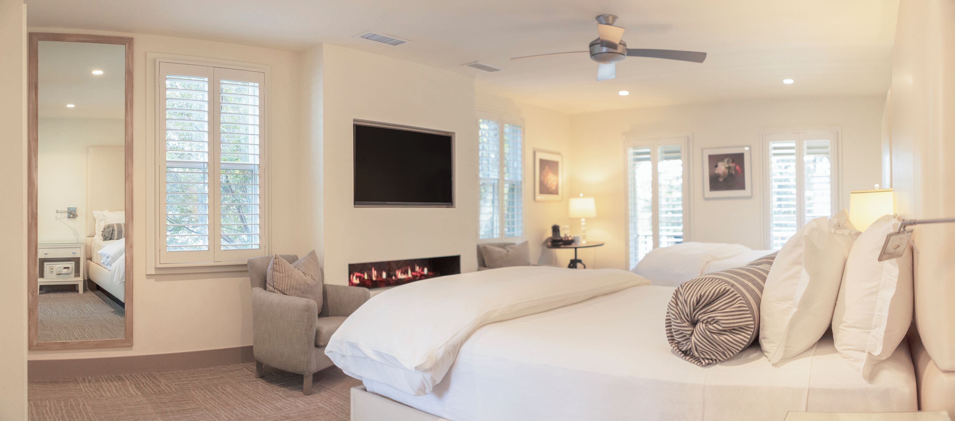 A hotel room with a bed, a chair, a TV, a fireplace, and large windows.