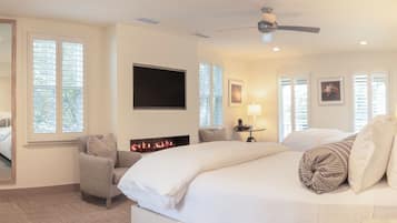 A hotel room with a bed, a chair, a TV, a fireplace, and large windows.