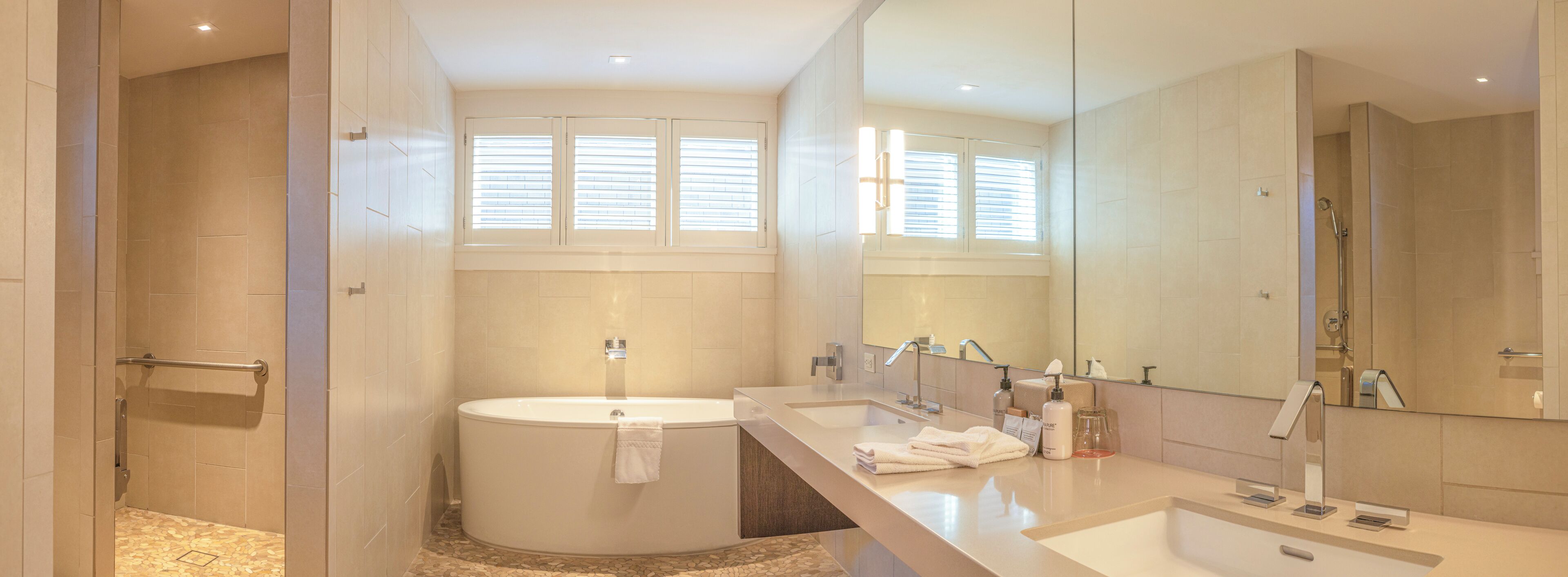 A modern bathroom with a bathtub, two sinks, a large mirror, and a shower area.