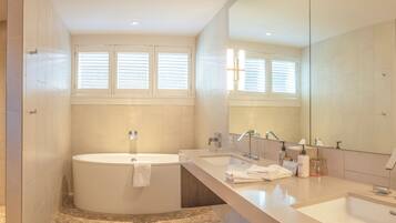A modern bathroom with a bathtub, two sinks, a large mirror, and a shower area.
