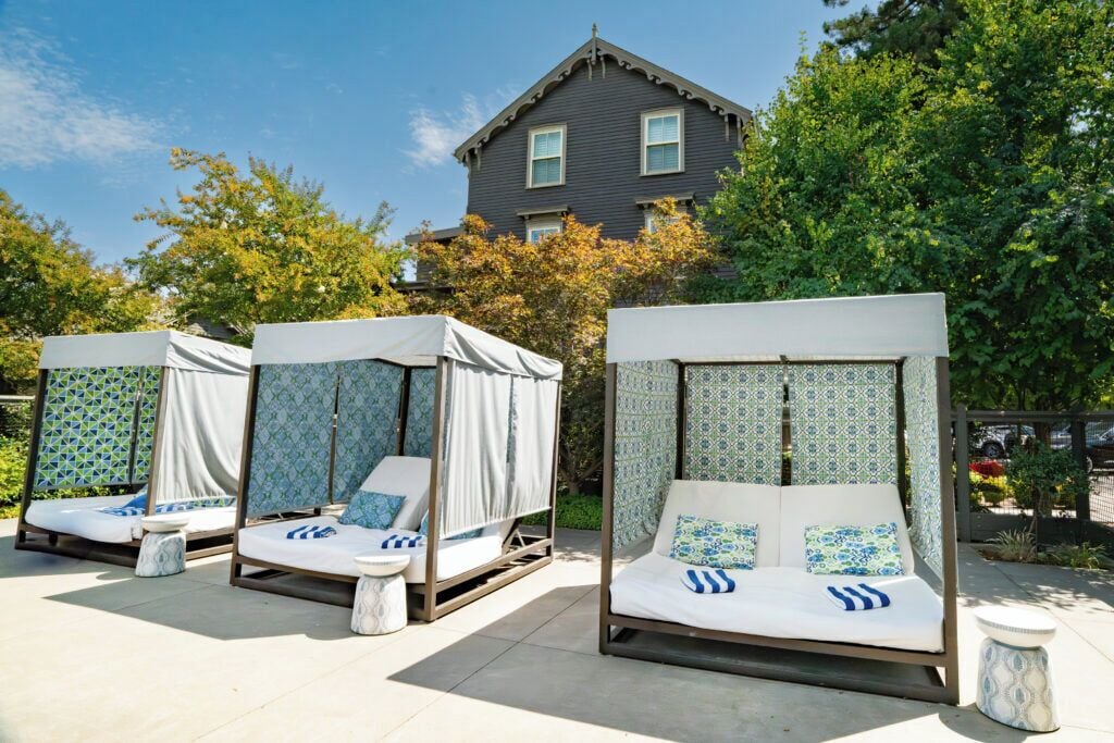 A set of four outdoor beds with canopies, arranged in a row with a house in the background.