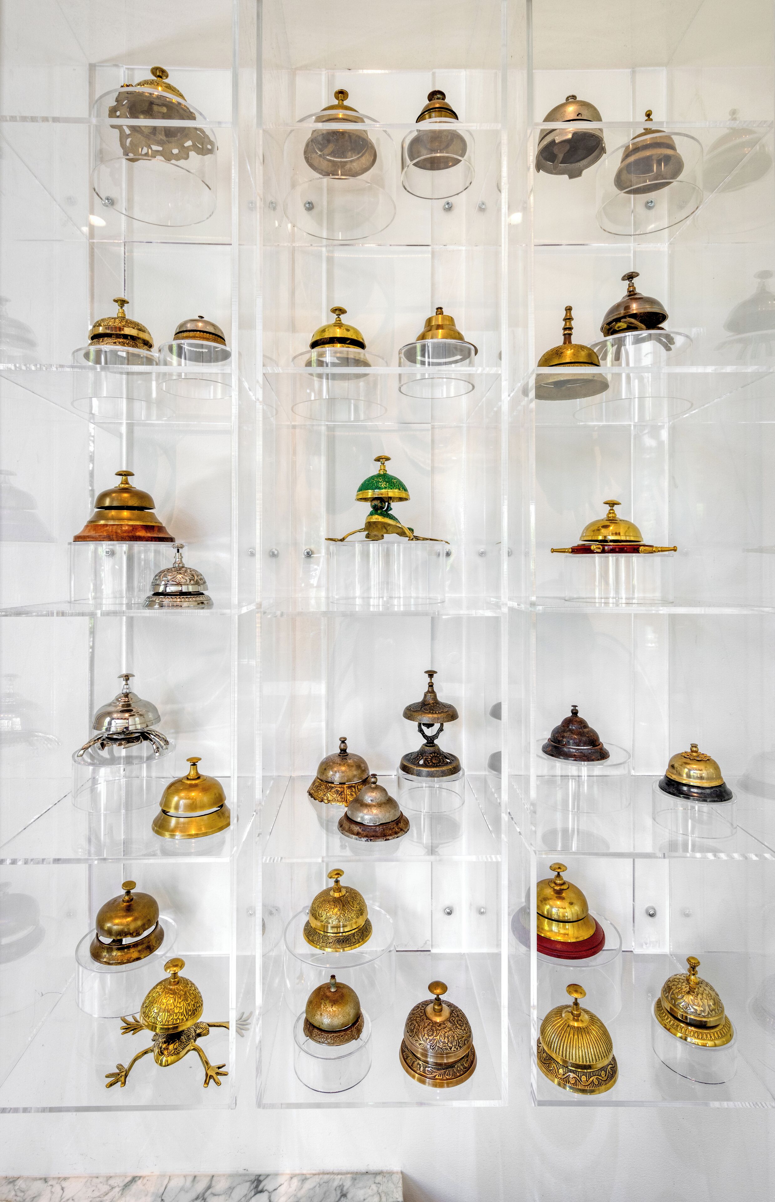 A display of various antique bells in clear cases, arranged in multiple rows and columns.