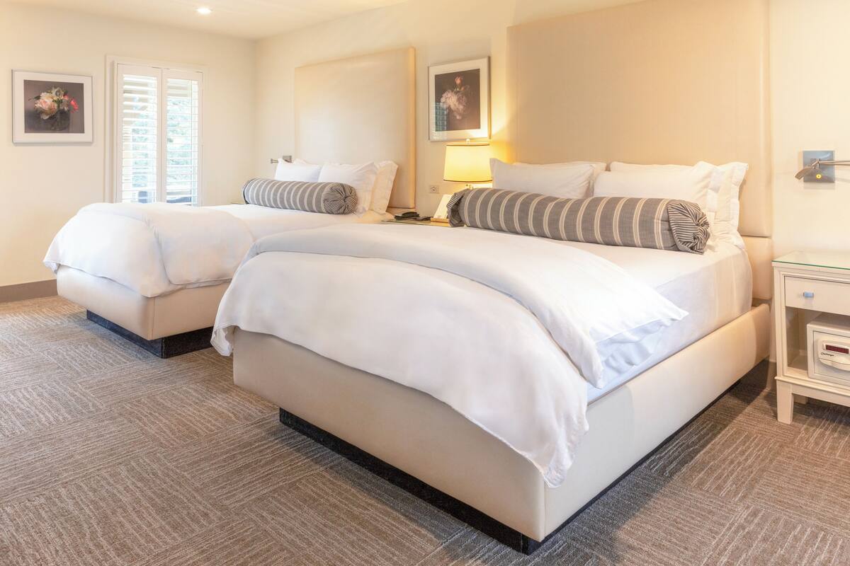 A hotel room with two beds, a ceiling fan, a nightstand, and a bedside table.
