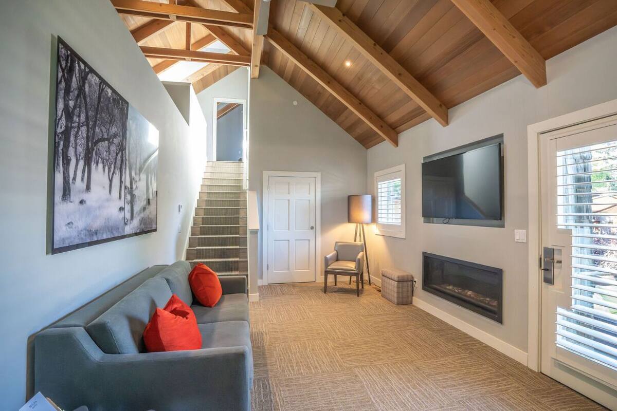 A modern living room with a grey sofa, red cushions, a fireplace, a TV, and a staircase leading to another level.