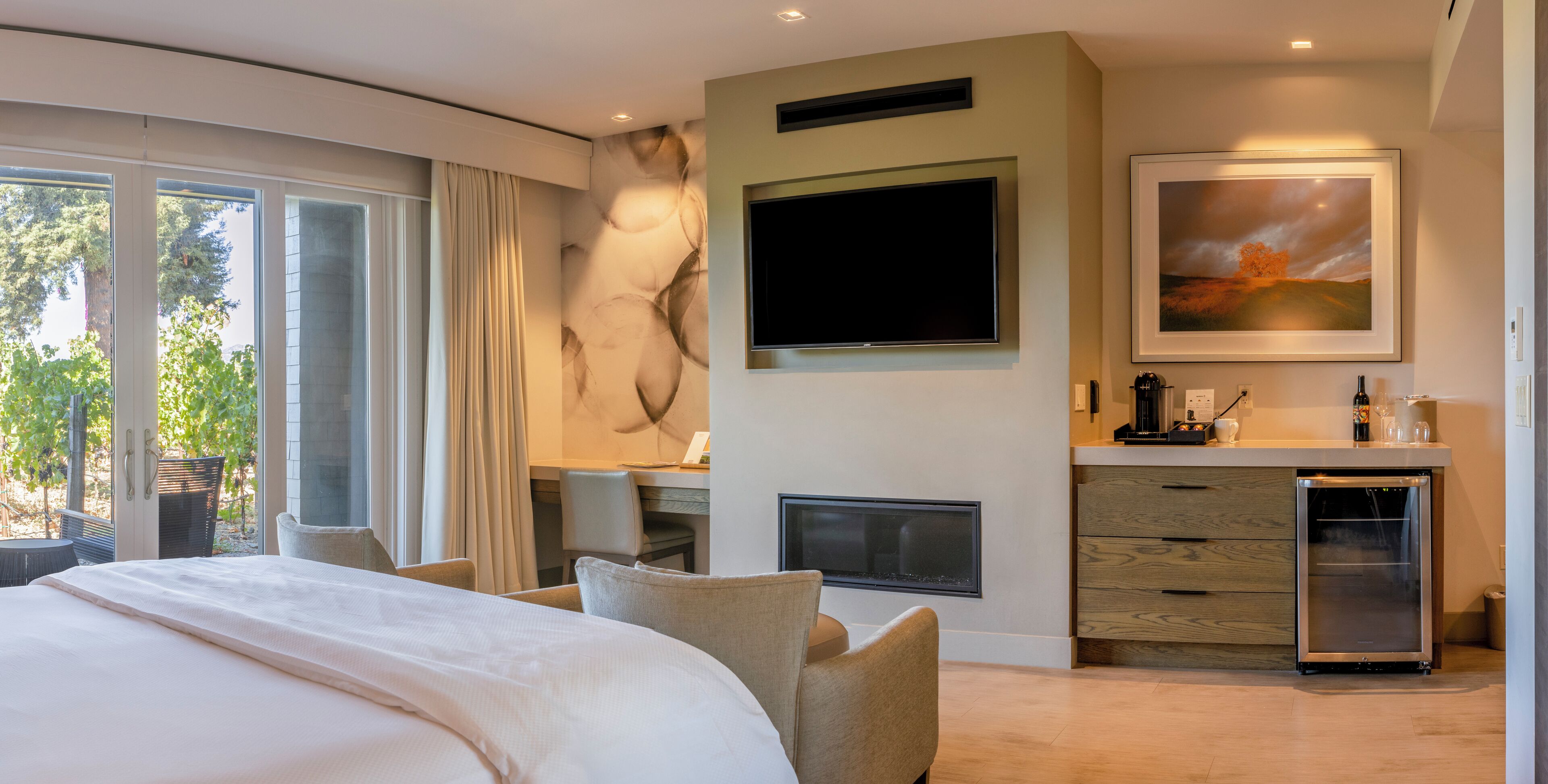 Une chambre d’hôtel moderne dotée d’un grand lit, d’un bureau, d’une télévision à écran plat, d’une cheminée et d’un petit réfrigérateur.