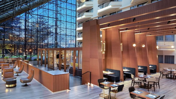 A modern hotel lobby with a glass atrium, wooden paneling, and seating areas.