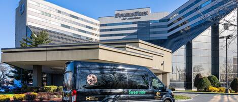 A black van parked in front of a hotel with a modern design, a sign reading "DOUBLETREE", and a "Sweet Ride" logo on the side.