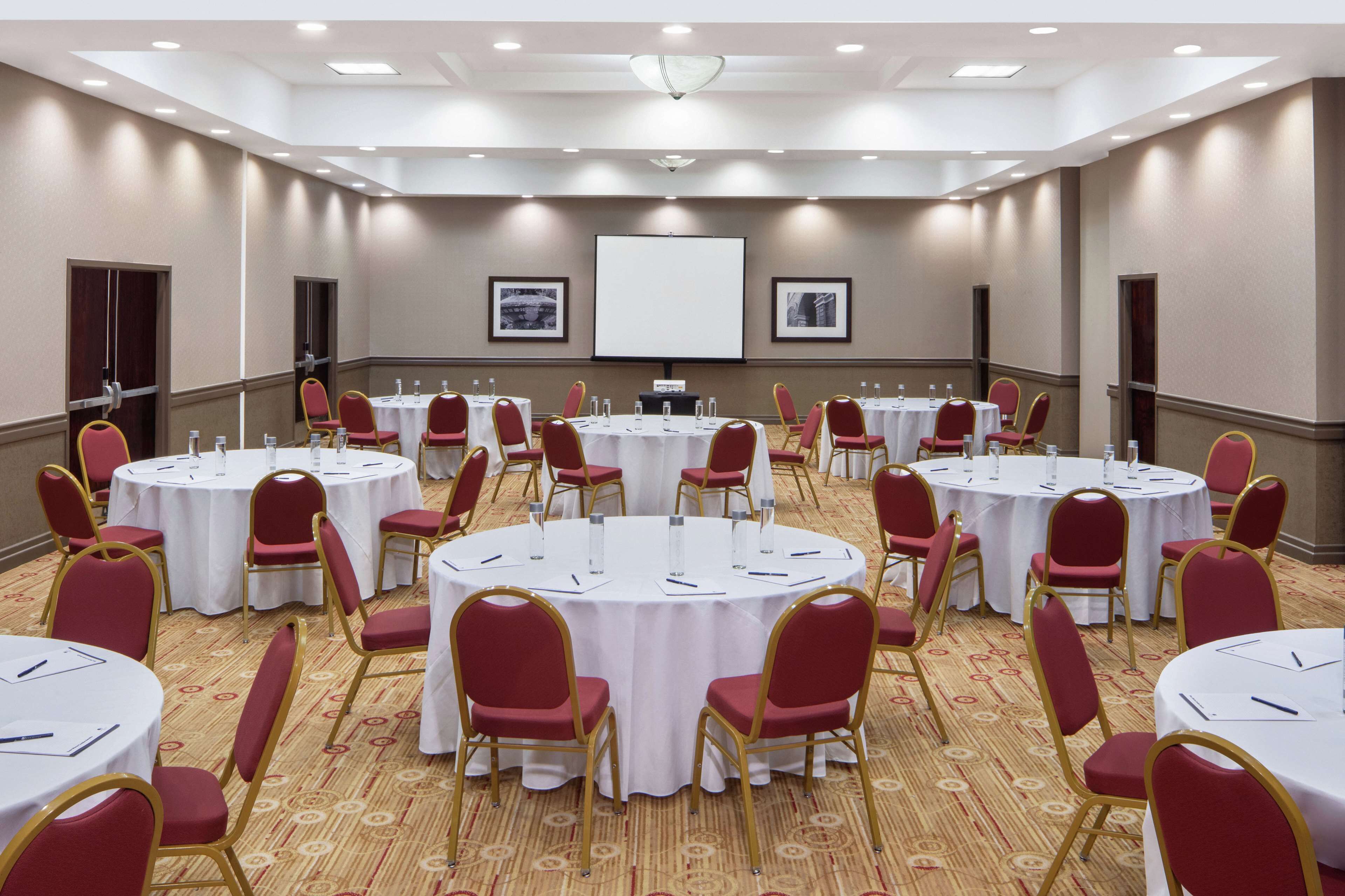A conference room with multiple round tables, red chairs, and a large screen at the front.
