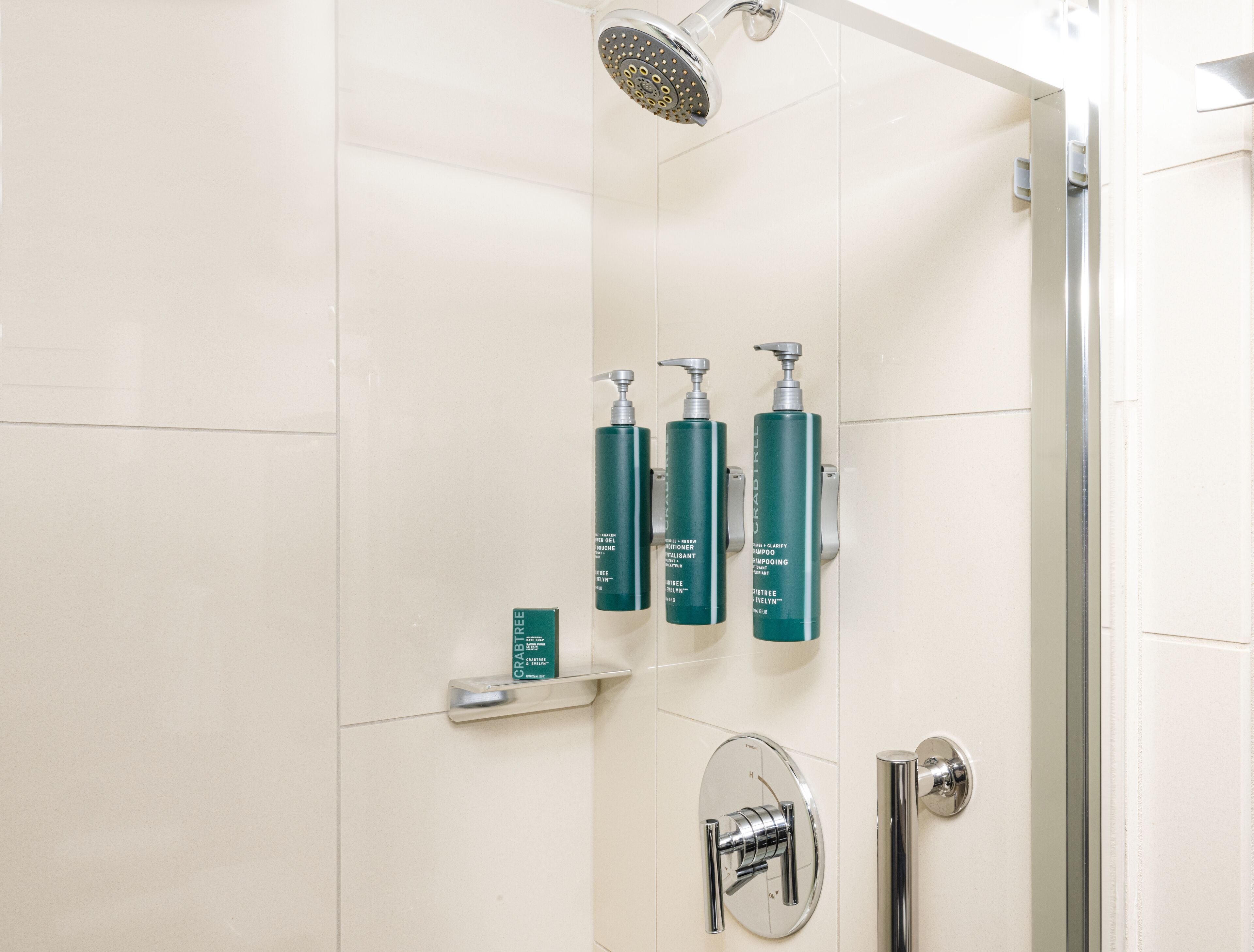 Une salle de bain moderne avec une douche, trois flacons verts de shampoing Crabtree et un robinet chromé.