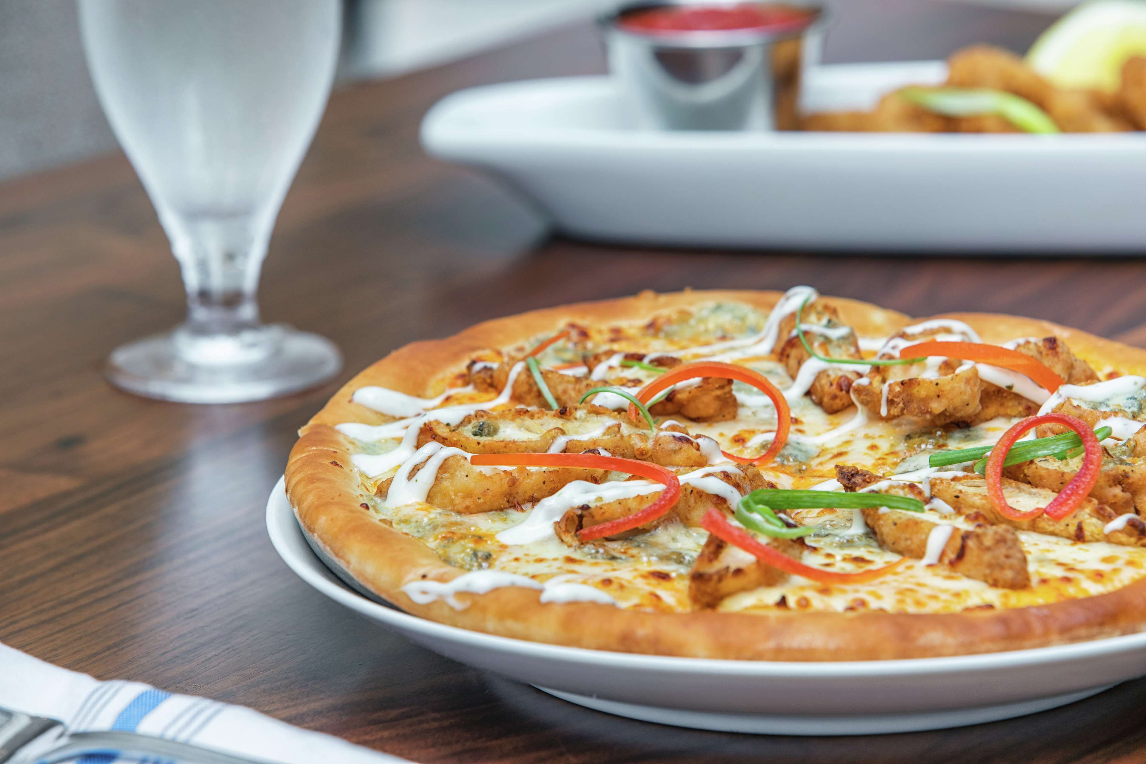 Une pizza garnie et un verre d’eau sur une table.